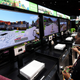 A row of gamers wearing ear phones and holding Xbox controllers sit in front of screens showing minecraft gameplay.